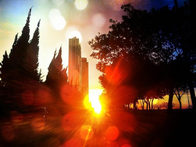 A bustling city skyline at dusk, with pockets of glowing heat representing the urban heat island effect, contrasting with cooler surrounding natural areas.